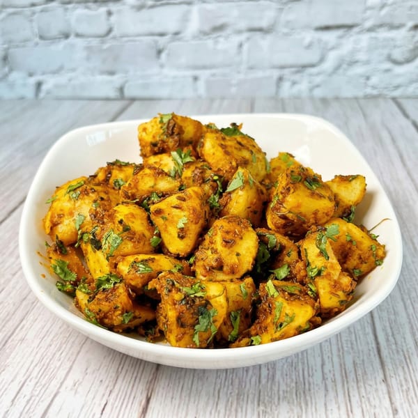 A white bowl filled with golden Indian spiced potatoes, garnished with fresh green cilantro.