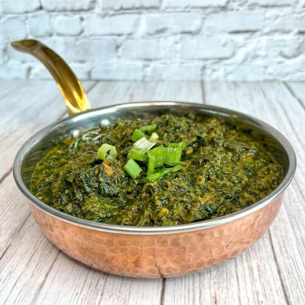 Indian palak paneer, a vibrant green spinach dish with paneer cheese, in a copper serving pan.