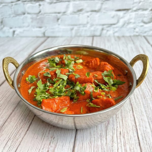 Spice Hub's vibrant red Indian curry with chicken pieces, garnished with fresh cilantro in a metal bowl.